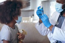 Médecin afro-américain se préparant à vacciner son enfant patient. rester à la maison en isolement personnel pendant le confinement en quarantaine. — Photo de stock