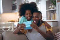African american girl standing in living room giving her father a present. staying at home in self isolation during quarantine lockdown. — Stock Photo