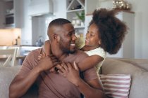 African american man and his daughter embracing on couch. staying at home in self isolation during quarantine lockdown. — Stock Photo