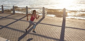 African american woman concentrating exercising on a promenade by the sea running. Fitness healthy outdoor lifestyle. — Stock Photo