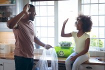 Menina afro-americana e seu pai triagem reciclagem juntos na cozinha. ficar em casa em auto-isolamento durante o confinamento de quarentena. — Fotografia de Stock