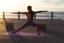 Donna afroamericana che si esercita sul lungomare vicino al mare facendo yoga. fitness stile di vita sano all'aperto. — Foto stock