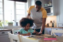 African american girl doing homework with her father. staying at home in self isolation during quarantine lockdown. — Stock Photo