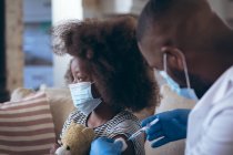 Médico afroamericano vacunando a su hijo paciente. permanecer en casa en aislamiento durante el bloqueo de cuarentena. - foto de stock