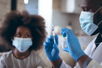 Médico afro-americano se preparando para vacinar seu filho paciente. ficar em casa em auto-isolamento durante o confinamento de quarentena. — Fotografia de Stock