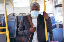 African american senior man wearing face mask standing on bus. digital nomad out and about in the city during coronavirus covid 19 pandemic. — Stock Photo