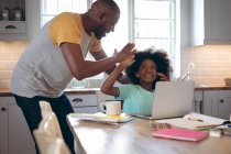 African american girl using laptop with her father. staying at home in self isolation during quarantine lockdown. — Stock Photo