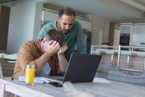 Casal masculino gay multi étnico preocupado passando por contas e usando laptop em casa. Ficar em casa em auto-isolamento durante o bloqueio de quarentena. — Fotografia de Stock