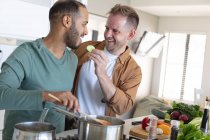Многонациональная гей-пара улыбается и готовит еду вместе дома. Оставаться дома в изоляции во время карантинной изоляции. — стоковое фото