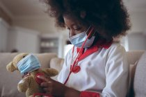 Afroamerikanerin spielt Ärztin und Patientin mit ihrem Teddy. Während der Quarantäne zu Hause bleiben und sich selbst isolieren. — Stockfoto