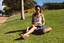 Afroamerikanerin sitzt auf Gras und runzelt die Stirn, liest im Park ein Buch. Freizeitgestaltung. — Stockfoto