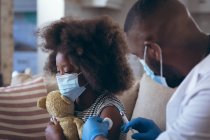 Médecin afro-américain vaccinant son enfant patient. rester à la maison en isolement personnel pendant le confinement en quarantaine. — Photo de stock