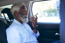 Africano americano idoso sentado em táxi táxi falando no smartphone. nômade digital para fora e sobre na cidade. — Fotografia de Stock