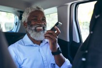 Африканський старший американець сидить у таксі і розмовляє по смартфону і посміхається. Цифровий кочівник і все в місті. — стокове фото