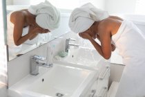 Afroamerikanerin wäscht ihre Gesichtsmaske im Waschbecken im Badezimmer ab. Zu Hause bleiben in Selbstisolierung in Quarantäne — Stockfoto