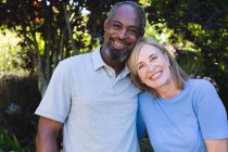 Portrait of diverse senior couple in garden looking at camera and smiling. staying at home in isolation during quarantine lockdown. — Stock Photo