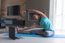 African american woman practicing yoga while looking at laptop screen at home. staying at home in self isolation in quarantine lockdown — Stock Photo