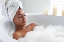 Mujer afroamericana relajándose en la bañera en el baño. permaneciendo en casa en aislamiento en cuarentena - foto de stock