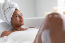 Mulher afro-americana atenciosa relaxando na banheira no banheiro. ficar em casa em auto-isolamento em quarentena — Fotografia de Stock