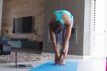 Mujer afroamericana practicando yoga frente a la laptop en casa. permaneciendo en casa en aislamiento en cuarentena - foto de stock