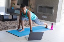 African american woman practicing yoga while looking at laptop screen at home. staying at home in self isolation in quarantine lockdown — Stock Photo