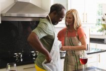 Diverse senior couple putting on aprons in kitchen before cooking. staying at home in isolation during quarantine lockdown. — Stock Photo