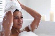 Thoughtful african american woman relaxing in bathtub at bathroom. staying at home in self isolation in quarantine lockdown — Stock Photo