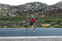 Afroamerikanischer Mann beim Outdoor-Laufen auf einer Küstenstraße. Fitnesstraining und gesunder Lebensstil im Freien. — Stockfoto