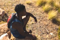 Uomo afroamericano che si allena all'aperto seduto su una roccia su una montagna. allenamento fitness e stile di vita sano all'aperto. — Foto stock