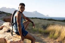 Homem afro-americano se exercitando ao ar livre sentado na rocha em uma montanha. treinamento de fitness e estilo de vida saudável ao ar livre. — Fotografia de Stock