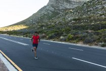 Hombre afroamericano haciendo ejercicio al aire libre corriendo por una carretera costera. entrenamiento de fitness y estilo de vida saludable al aire libre. - foto de stock