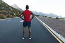 Hombre afroamericano haciendo ejercicio al aire libre parado en una carretera costera. entrenamiento de fitness y estilo de vida saludable al aire libre. - foto de stock