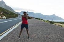 Un Afro-Américain qui fait de l'exercice en plein air sur une route côtière. entraînement physique et mode de vie sain en plein air. — Photo de stock