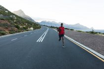 Un Afro-Américain faisant de l'exercice en plein air sur une route côtière. entraînement physique et mode de vie sain en plein air. — Photo de stock