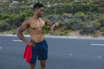 Африканський американець, що займається спортом, перевіряє смартв на прибережній дорозі. Тренування фітнесу і здоровий спосіб життя на вулиці. — стокове фото