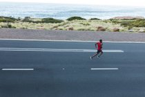 Hombre afroamericano haciendo ejercicio al aire libre corriendo por una carretera costera. entrenamiento de fitness y estilo de vida saludable al aire libre. - foto de stock