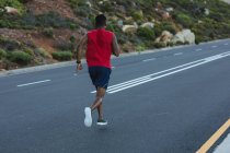 Afroamerikanischer Mann beim Outdoor-Laufen auf einer Küstenstraße. Fitnesstraining und gesunder Lebensstil im Freien. — Stockfoto