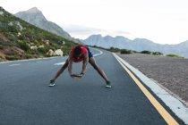 Afrikanischer Mann beim Dehnen im Freien auf einer Küstenstraße. Fitnesstraining und gesunder Lebensstil im Freien. — Stockfoto