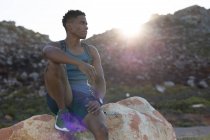 Afroamerikanischer Mann beim Sport im Freien auf einem Felsen an einer Küstenstraße sitzend. Fitnesstraining und gesunder Lebensstil im Freien. — Stockfoto