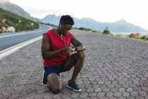 Uomo afroamericano che si allena all'aperto controllando smartwatch su una strada costiera. allenamento fitness e stile di vita sano all'aperto. — Foto stock
