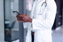 Mittelteil eines afrikanisch-amerikanischen Arztes mit weißem Mantel und Stethoskop mittels digitalem Tablet. Mediziner bei der Arbeit. — Stockfoto