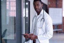 Retrato de un médico afroamericano con bata blanca y estetoscopio usando tableta digital. profesional médico en el trabajo. - foto de stock
