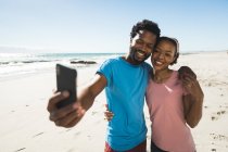 Щаслива афро-американська пара на пляжі біля моря робить сельфі. Здоровий вільний час на відкритому повітрі біля моря. — стокове фото