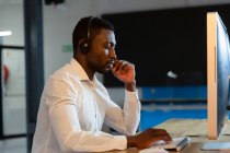 Homme d'affaires afro-américain occasionnel portant un casque de téléphone, en utilisant un ordinateur assis au bureau. homme d'affaires au travail dans un bureau moderne. — Photo de stock
