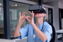 Médico femenino caucásico usando matorrales usando auriculares vr e interfaz virtual. profesional médico en el trabajo con tecnología. - foto de stock