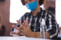 Mixed race businessman at the office wearing mask disinfecting hands. independent creative business during covid 19 coronavirus pandemic. — Stock Photo