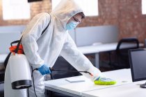 Reinigungskräfte in Hygieneanzügen, Handschuhen und Mundschutz desinfizieren Büro und Möbel. Arbeitsplatzhygiene während Coronavirus covid 19 Pandemie. — Stockfoto