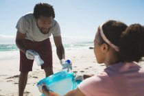 Африканская американская пара в латексных перчатках собирает мусор с пляжа. Охрана экологического пляжа — стоковое фото