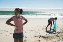 Couple de course afro-américain portant des masques faciaux collectant les déchets de la plage. éco plage conservation pendant coronavirus covid 19 pandémie. — Photo de stock