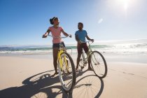 Happy african american couple on beach riding bicycle. healthy outdoor leisure time by the sea. — Stock Photo